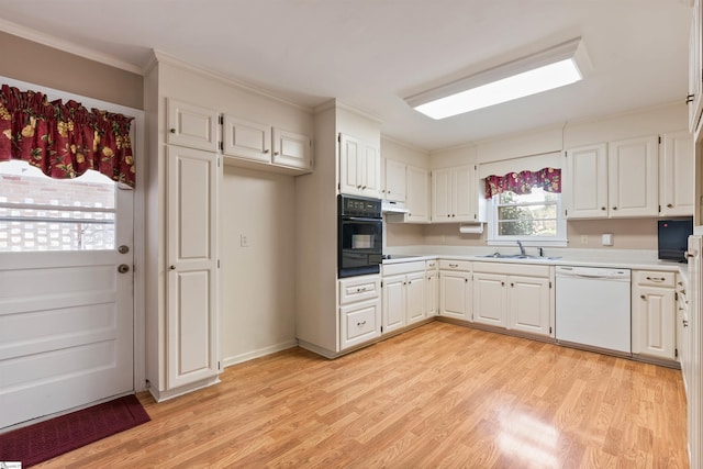 kitchen featuring black appliances, light wood-style flooring, a sink, white cabinetry, and light countertops