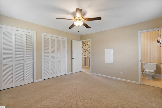 unfurnished bedroom with carpet, baseboards, ceiling fan, multiple closets, and ensuite bathroom