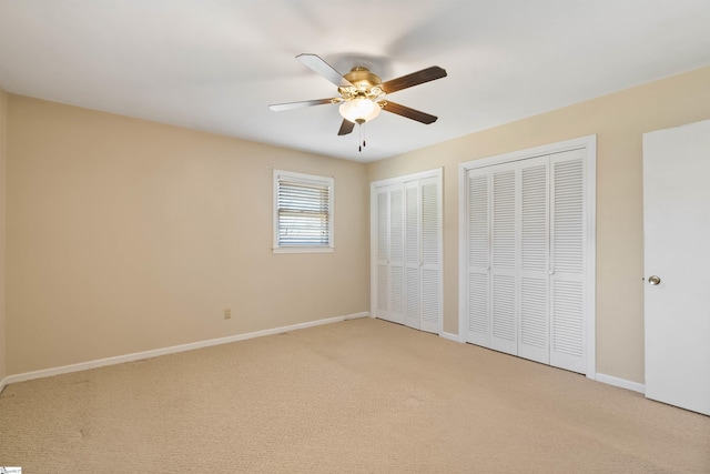 unfurnished bedroom with light colored carpet, two closets, baseboards, and ceiling fan