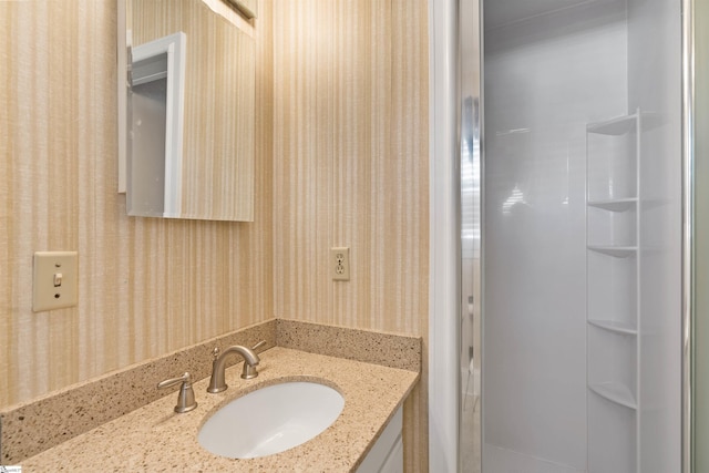 bathroom featuring wallpapered walls, a shower stall, and vanity