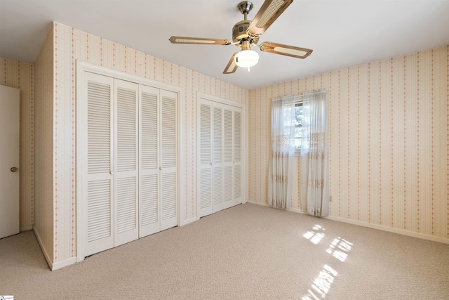 unfurnished bedroom featuring wallpapered walls, carpet flooring, baseboards, and two closets