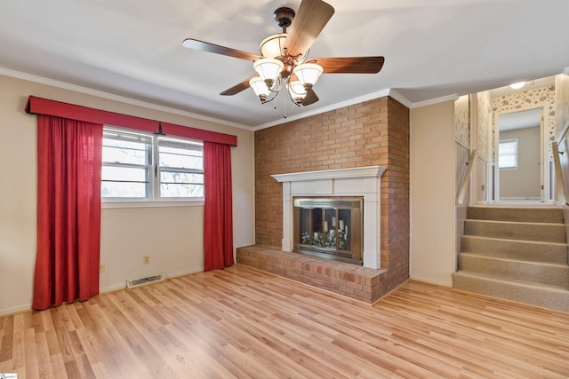 unfurnished living room featuring wood finished floors, visible vents, a fireplace, ornamental molding, and stairs