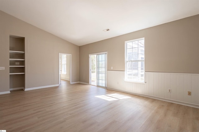 spare room featuring built in features, visible vents, light wood finished floors, vaulted ceiling, and wainscoting