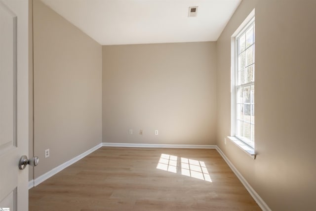 spare room featuring a wealth of natural light, light wood-type flooring, baseboards, and visible vents