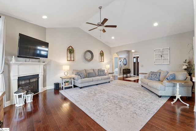 living area featuring a ceiling fan, hardwood / wood-style flooring, a glass covered fireplace, arched walkways, and lofted ceiling