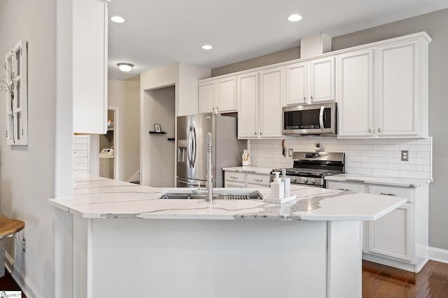 kitchen featuring stainless steel appliances, washer / clothes dryer, tasteful backsplash, and white cabinets