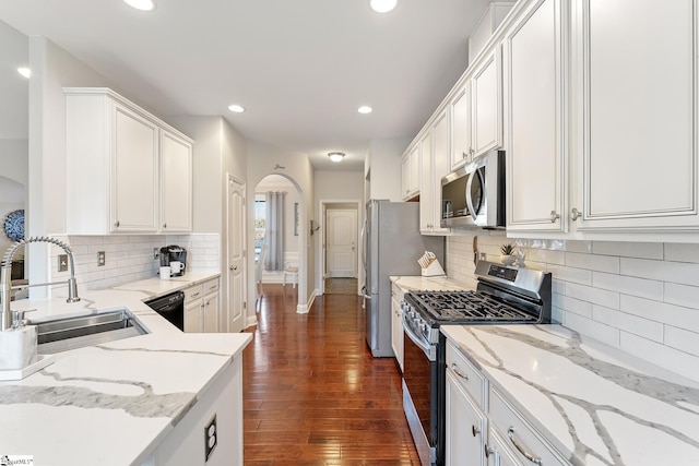 kitchen featuring dark wood-style floors, arched walkways, a sink, appliances with stainless steel finishes, and white cabinetry