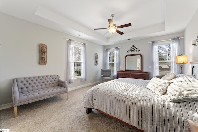 carpeted bedroom featuring a tray ceiling, multiple windows, baseboards, and visible vents