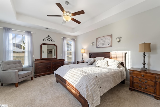 bedroom with ceiling fan, a tray ceiling, visible vents, and light carpet