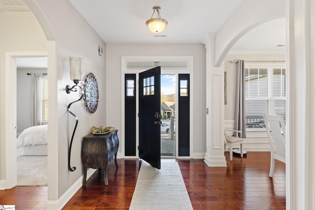 foyer with arched walkways, dark wood-style floors, visible vents, and a wealth of natural light