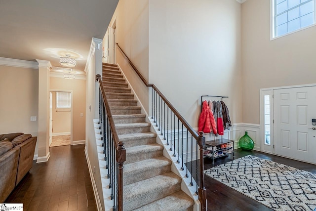 entrance foyer featuring a wainscoted wall, ornamental molding, dark wood finished floors, a towering ceiling, and stairs