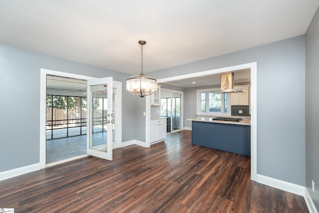 unfurnished dining area featuring dark wood-style floors, a notable chandelier, a wealth of natural light, and baseboards