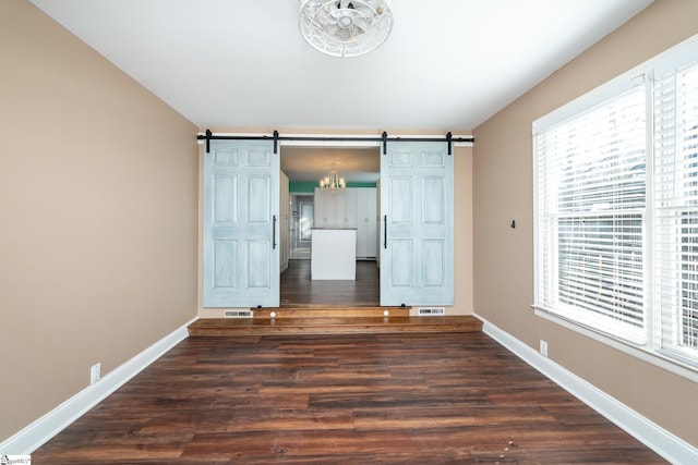 unfurnished room with a barn door, wood finished floors, visible vents, and baseboards