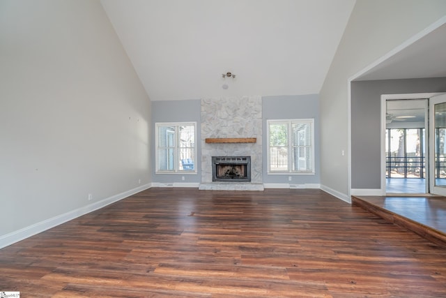 unfurnished living room featuring baseboards, high vaulted ceiling, a stone fireplace, and wood finished floors