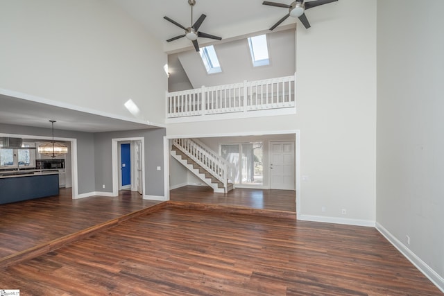 unfurnished living room featuring baseboards, dark wood-style flooring, a sink, stairs, and ceiling fan with notable chandelier