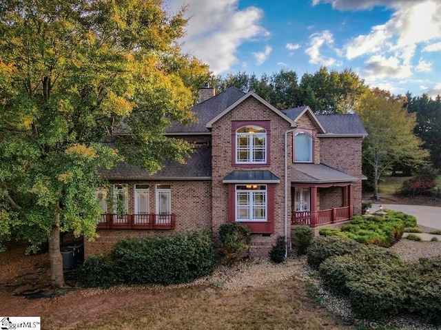 traditional-style home with brick siding, a porch, a chimney, and roof with shingles