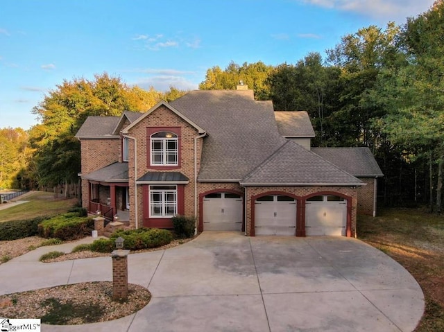 traditional-style house featuring a porch, a shingled roof, concrete driveway, a garage, and brick siding