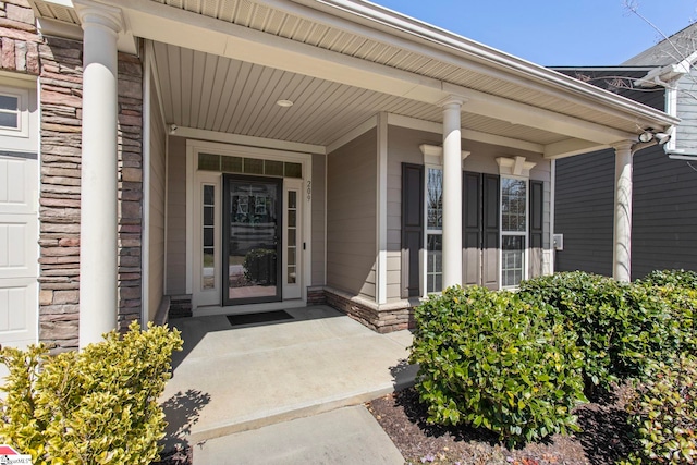 view of exterior entry with a garage, stone siding, brick siding, and a porch