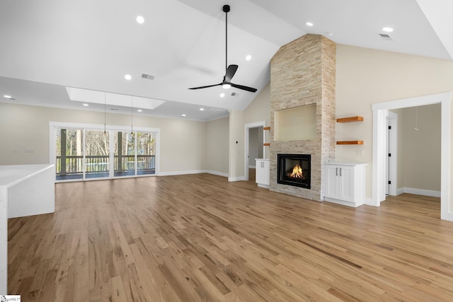 unfurnished living room featuring visible vents, high vaulted ceiling, light wood-style flooring, a stone fireplace, and ceiling fan