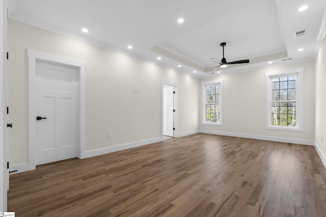 empty room with a tray ceiling, wood finished floors, recessed lighting, crown molding, and baseboards