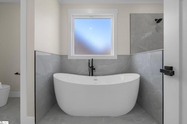 full bath with marble finish floor, walk in shower, a freestanding bath, and toilet