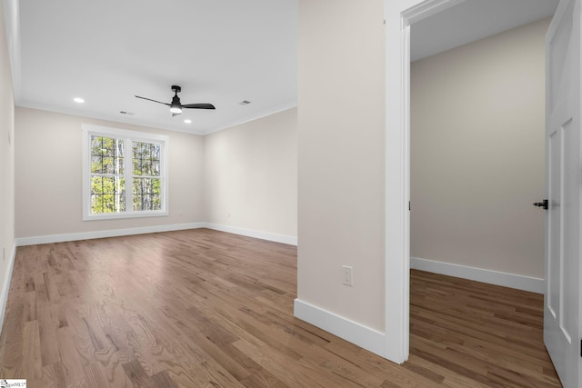 empty room with crown molding, light wood-style flooring, a ceiling fan, and baseboards