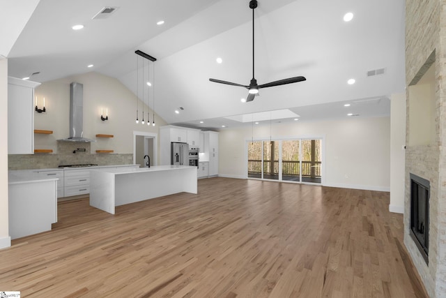 unfurnished living room featuring high vaulted ceiling, a fireplace, ceiling fan, a sink, and light wood-type flooring