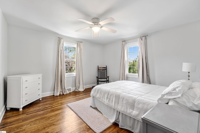 bedroom with multiple windows, a ceiling fan, baseboards, and wood finished floors