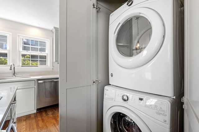 laundry area with dark wood finished floors, laundry area, stacked washer and clothes dryer, and a sink