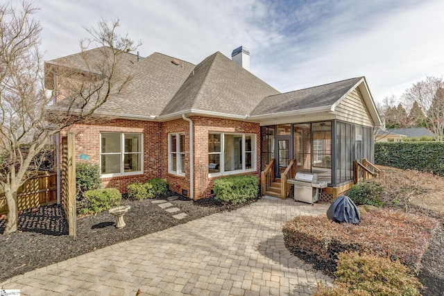 back of property with fence, roof with shingles, a sunroom, a chimney, and brick siding