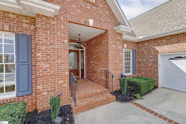 doorway to property with an attached garage, brick siding, and a shingled roof