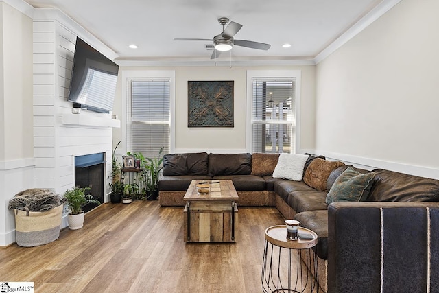 living area with wood finished floors, a ceiling fan, a fireplace, recessed lighting, and ornamental molding