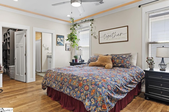 bedroom with a spacious closet, visible vents, crown molding, ensuite bathroom, and wood finished floors