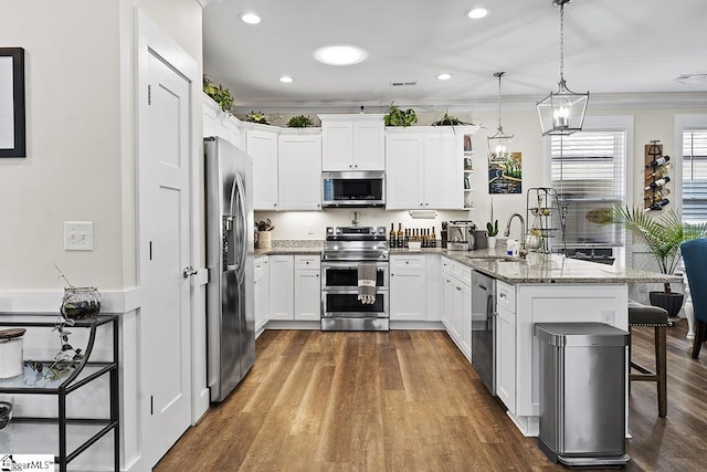 kitchen featuring a peninsula, a sink, white cabinets, appliances with stainless steel finishes, and a kitchen breakfast bar