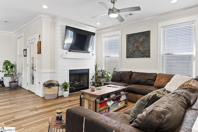 living area featuring visible vents, crown molding, light wood-style flooring, a fireplace, and a ceiling fan