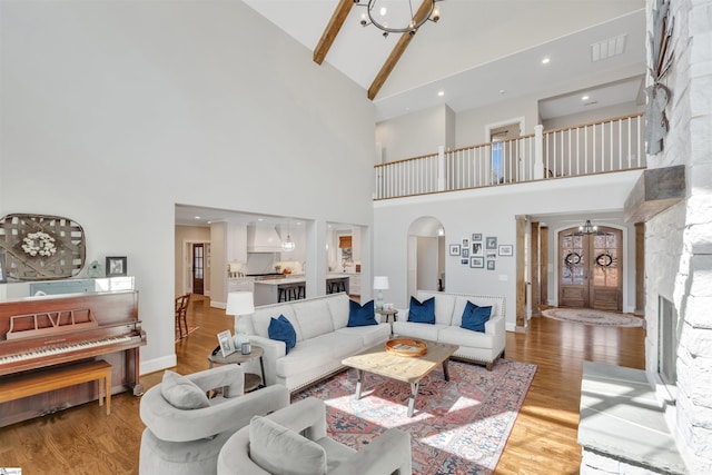 living area featuring visible vents, a notable chandelier, high vaulted ceiling, arched walkways, and light wood finished floors