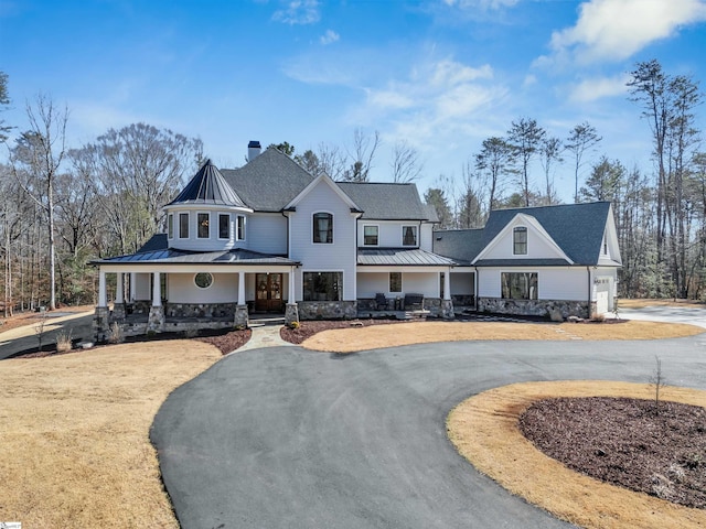 view of front of house with a porch, metal roof, stone siding, driveway, and a standing seam roof