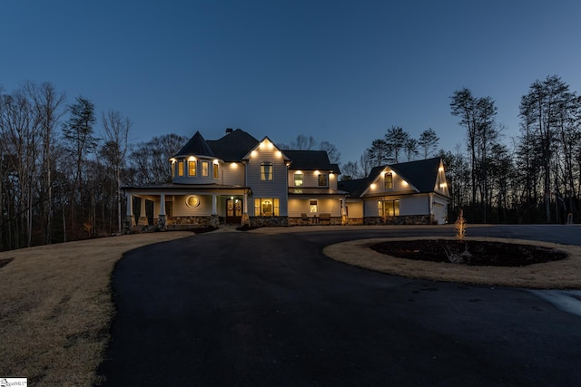 view of front facade with stone siding, curved driveway, and a porch