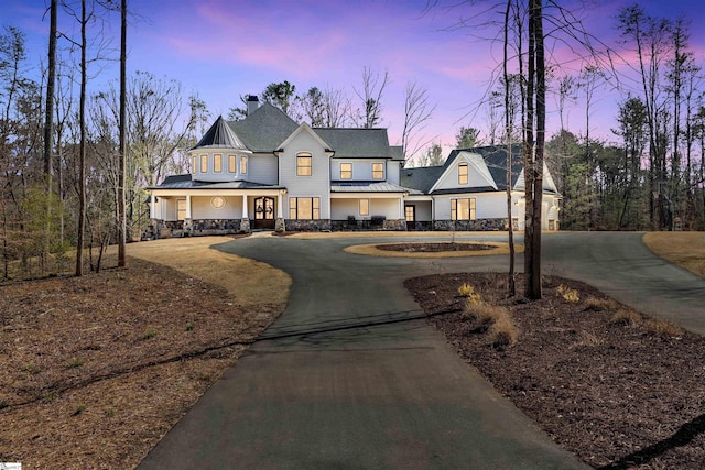 modern inspired farmhouse featuring a standing seam roof, stone siding, curved driveway, metal roof, and a chimney