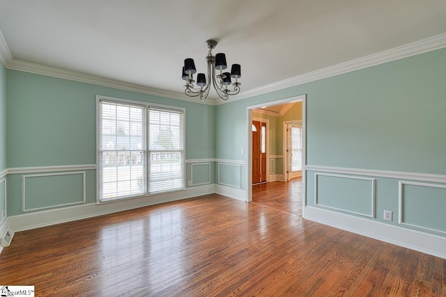 empty room featuring a chandelier, a decorative wall, crown molding, and wood finished floors