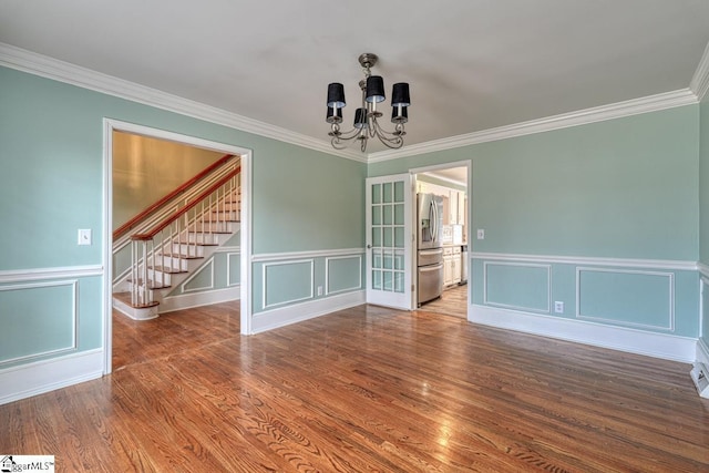 spare room featuring a chandelier, stairs, ornamental molding, wood finished floors, and a decorative wall