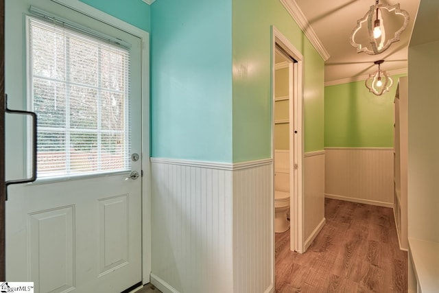 entryway with crown molding, a wainscoted wall, and light wood finished floors