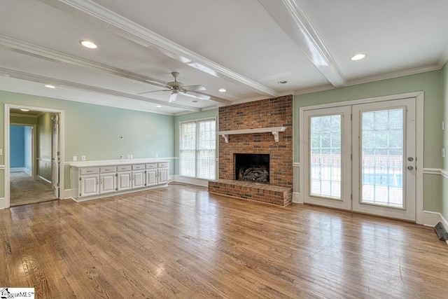 unfurnished living room featuring beamed ceiling, a brick fireplace, wood finished floors, and ornamental molding