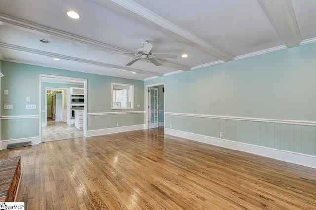 spare room featuring beamed ceiling, ornamental molding, wainscoting, wood finished floors, and a ceiling fan