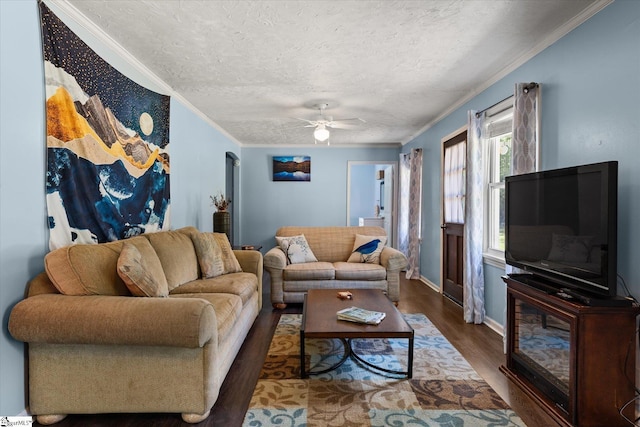 living area featuring wood finished floors, baseboards, ceiling fan, a textured ceiling, and crown molding