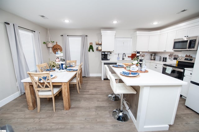 kitchen featuring a breakfast bar area, visible vents, a sink, stainless steel appliances, and light wood-style floors