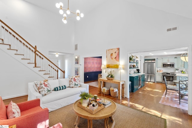 living room featuring visible vents, a chandelier, stairway, light wood-style flooring, and high vaulted ceiling