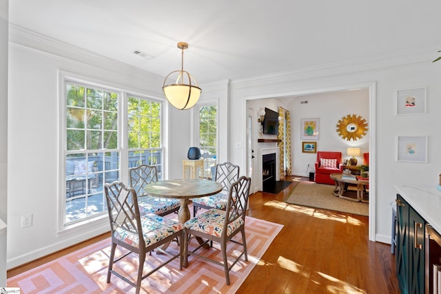 dining room featuring crown molding, a fireplace with flush hearth, wood finished floors, and plenty of natural light