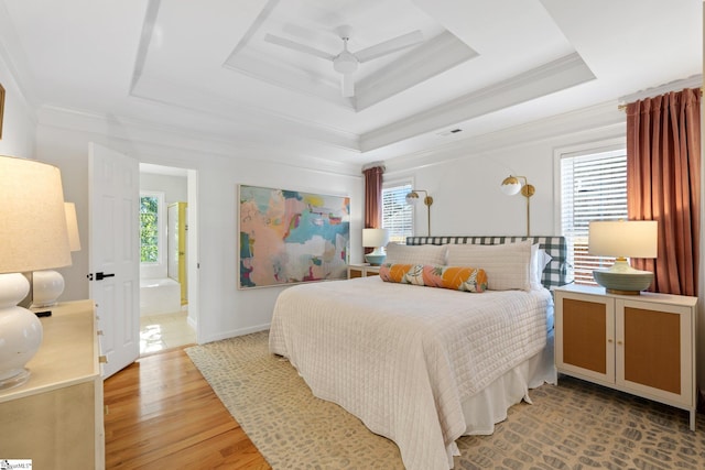 bedroom with a tray ceiling, multiple windows, light wood-type flooring, and ornamental molding