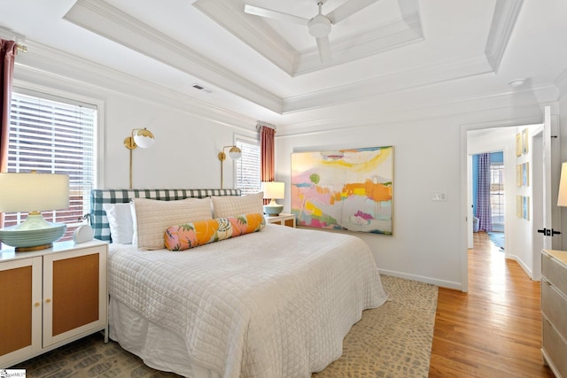 bedroom with visible vents, ornamental molding, wood finished floors, a raised ceiling, and a ceiling fan